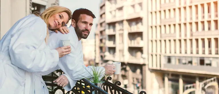 Zwei Personen stehen auf dem Balkon mit einem Kaffee in der Hand.