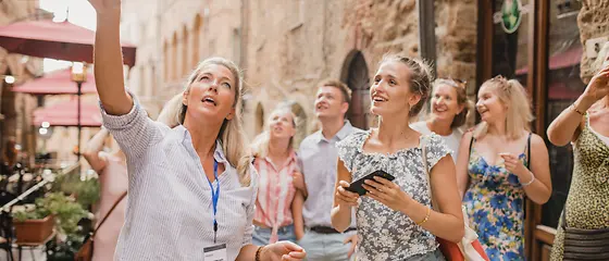 Reisegruppe in einer Altstadt - Reiseleiterversicherung Eine Reisegruppe befindet sich in einer Altstadt. Eine Frau zeigt mit ihrem Finger auf ein Gebäude.