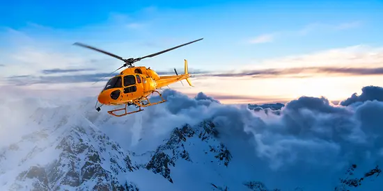 Ein gelber Helikopter fliegt bei Sonnenuntergang über die Rocky Mountains