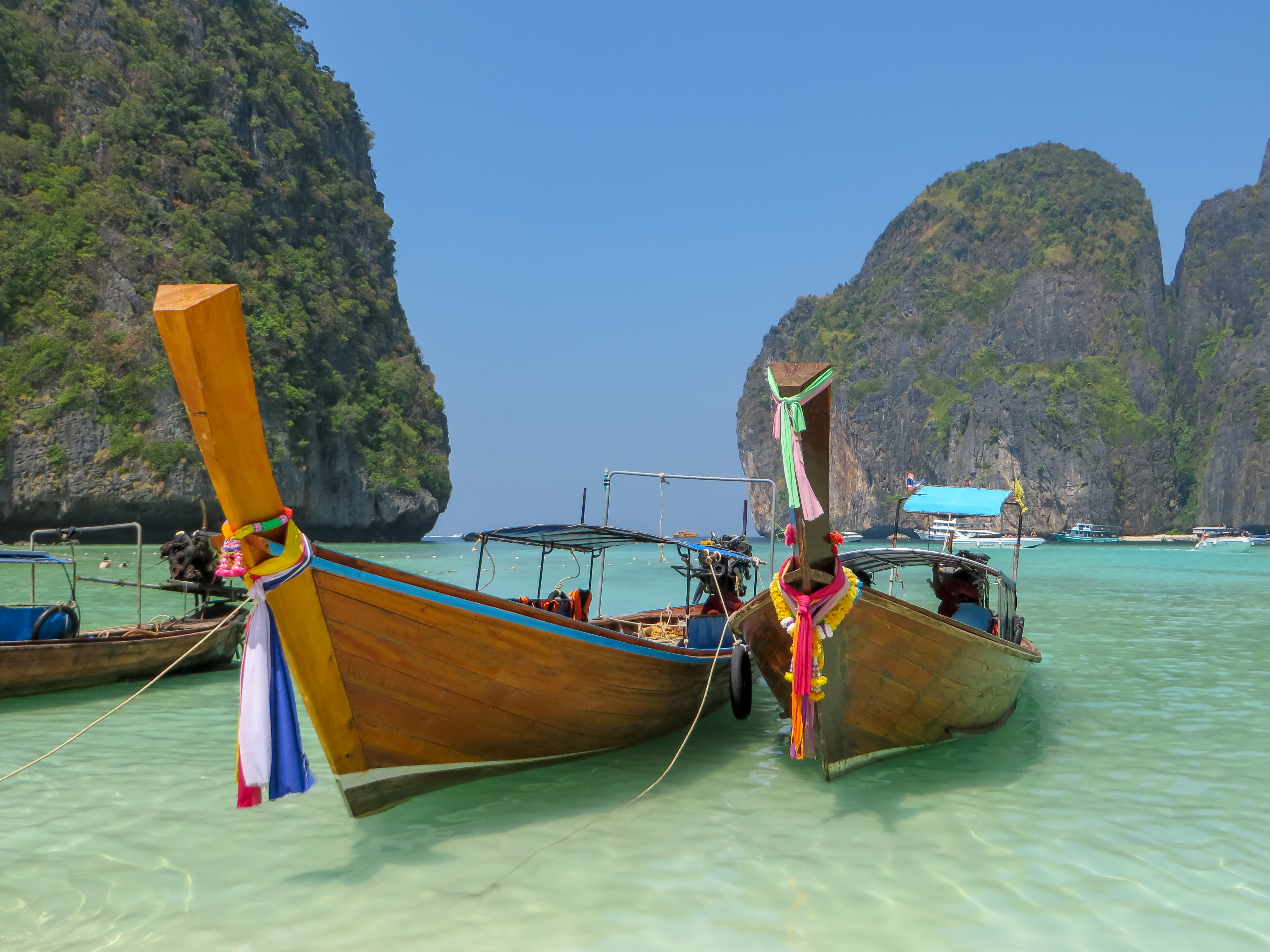 Zwei kleine Boote aus Holz liegen in einer Bucht. Rundherum ist türkises Wasser und riesige Felsen. 
