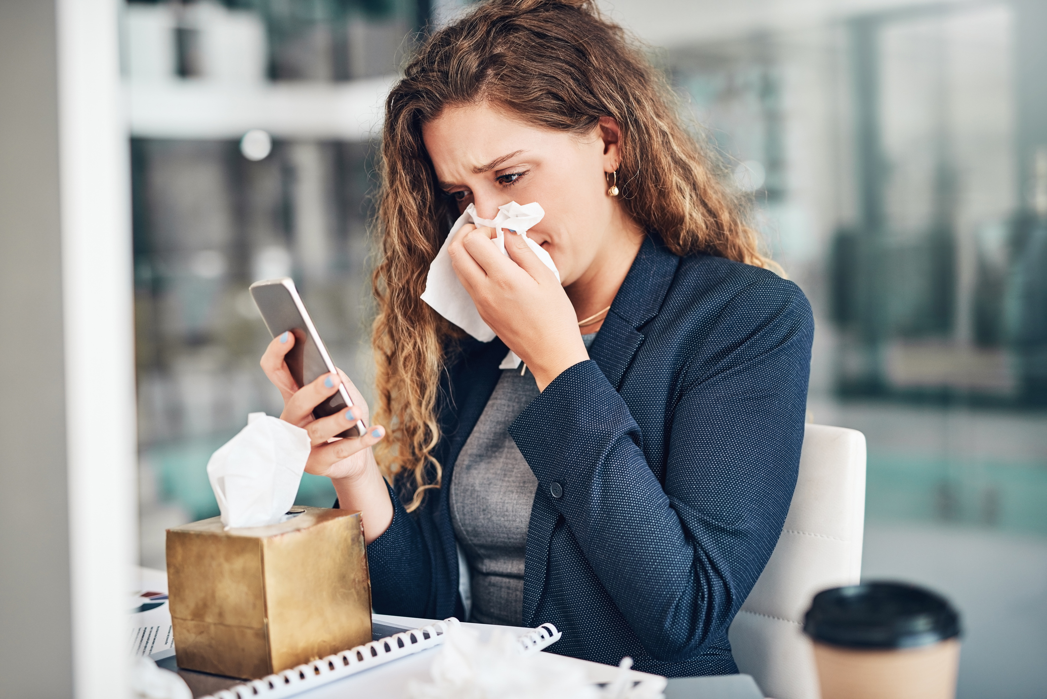A woman is holding a handkerchief to her nose and looking at her mobile phone