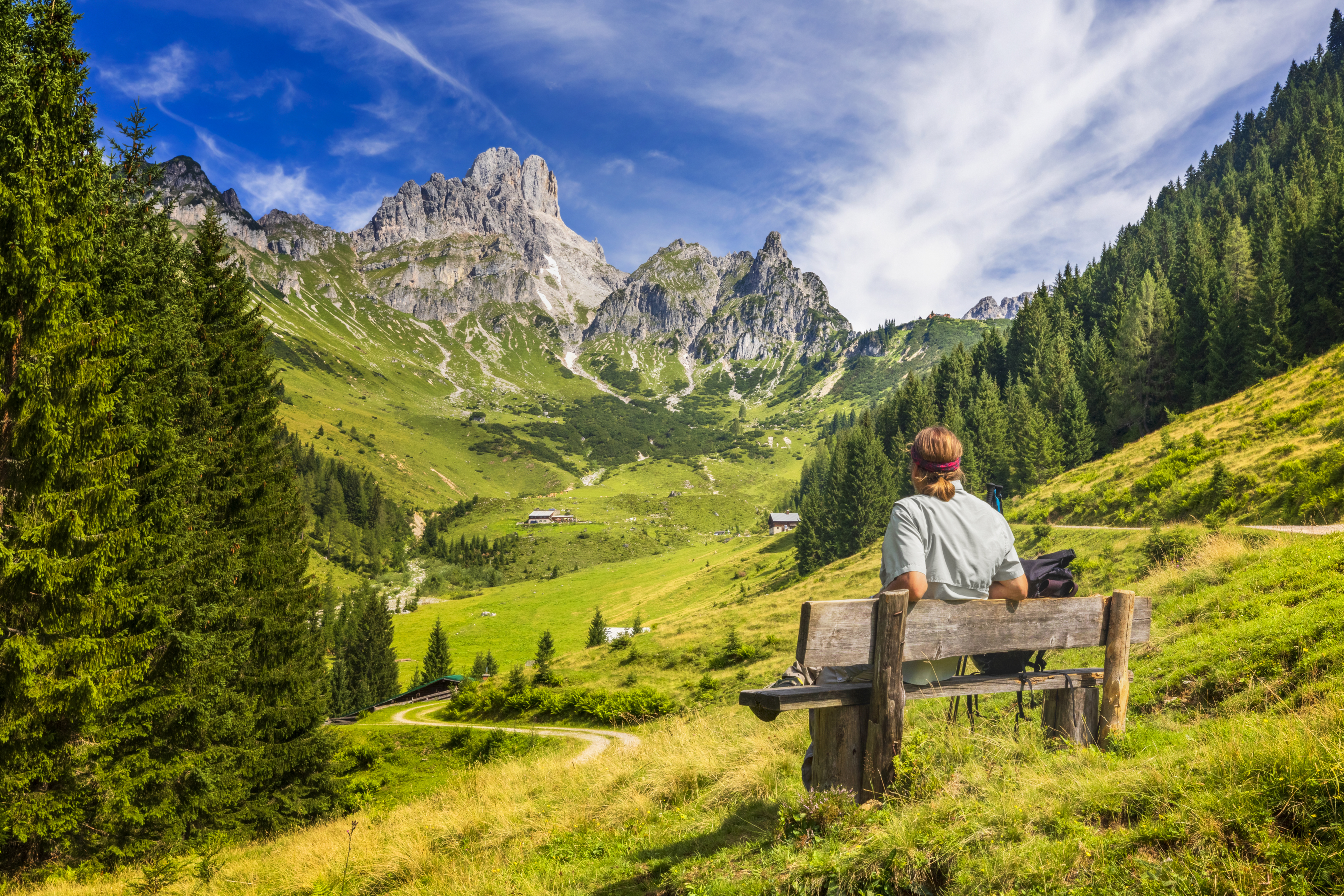 Ein Mensch sitzt auf einer Holzbank in den Alpen. Im Hintergrund sind Berge. 