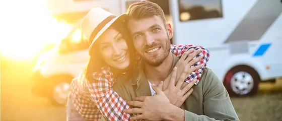 Pärchen am Wohnwagen - Miet-Camper-Schutz Ein Pärchen steht vor ihrem Wohnwagen und lächeln. Die Sonne geht gerade unter.
