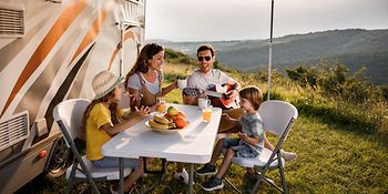 Mutter, Vater und ihre zwei Kinder sitzen an einem Campingtisch und singen. 