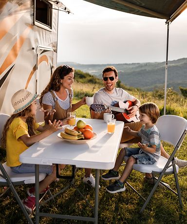 Mutter, Vater und ihre zwei Kinder sitzen an einem Campingtisch und singen. 