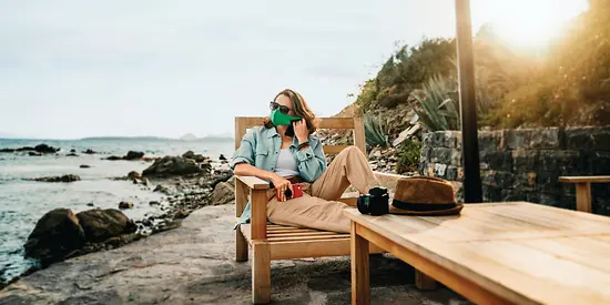Eine Frau liegt auf einer Liege und trägt eine grüne Maske. Im Hintergrund sieht man das Meer.