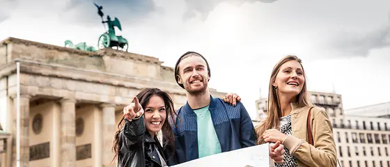 Drei Freunde stehen vor dem Brandenburger Tor und haben eine Karte in der Hand.