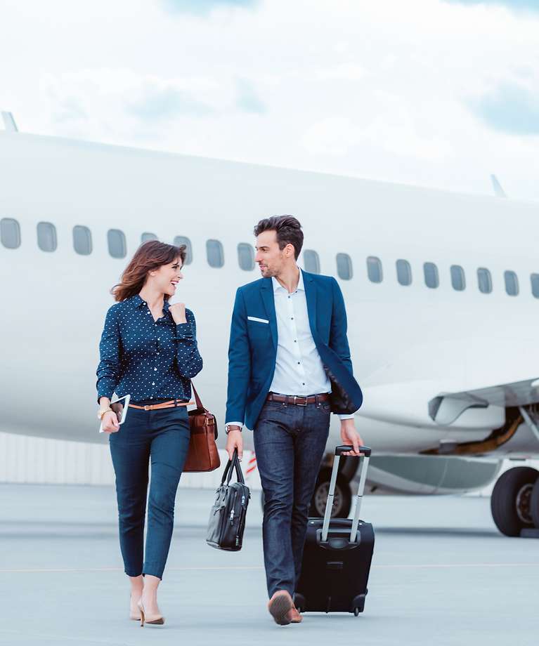 Eine Frau und ein Mann gehen auf dem Rollfeld am Flughafen. Im Hintergrund sieht man ein Flugzeug.