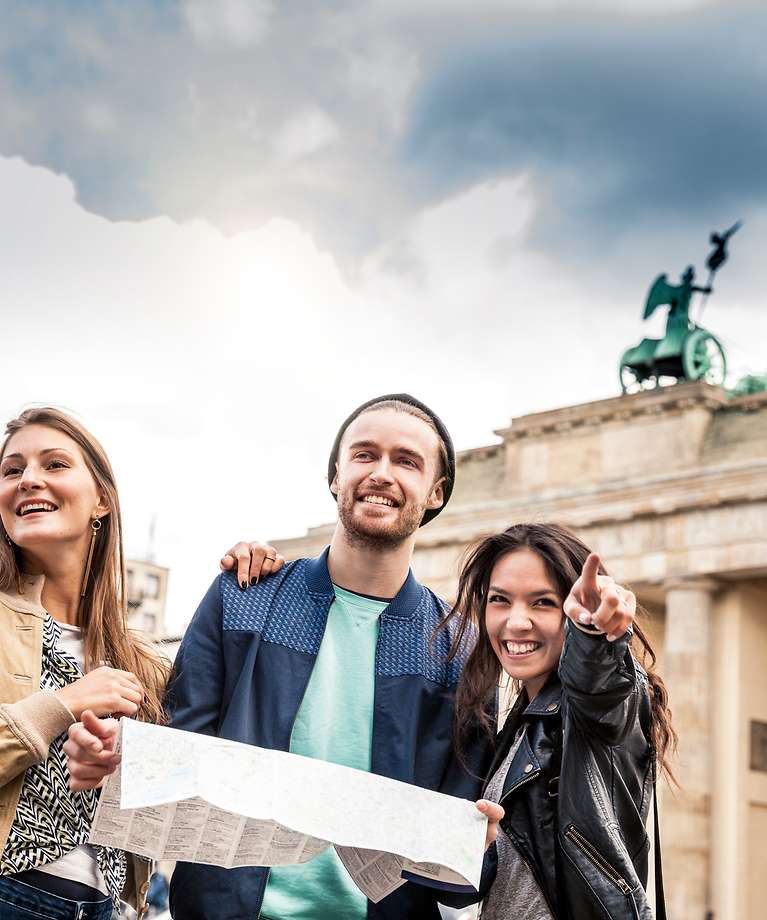 Drei Personen stehen mit einer Karte vor dem Brandenburger Tor. 