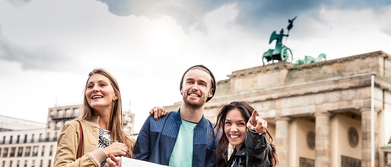 Drei Personen stehen mit einer Karte vor dem Brandenburger Tor. 