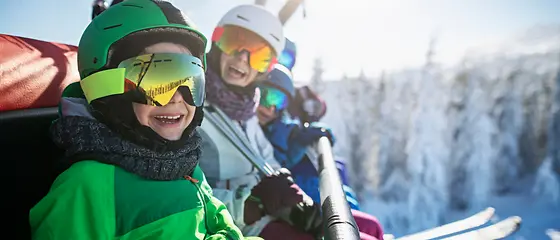 Familie im Skiurlaub - Aktivurlaub Plus Eine Familie sitzt im Skilift. Im Hintergrund sind verschneite Bäume zu sehen.