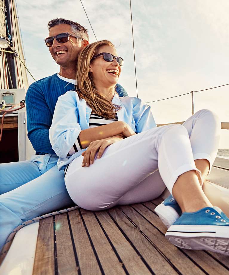 Ein Ehepaar sitzt auf einem Segelschiff. Der Mann hält seine Frau in den Armen.