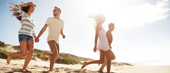 Vier Freunde am Strand - HanseMerkur Reiseversicherung Vier Freunde laufen am Strand in Richtung Wasser