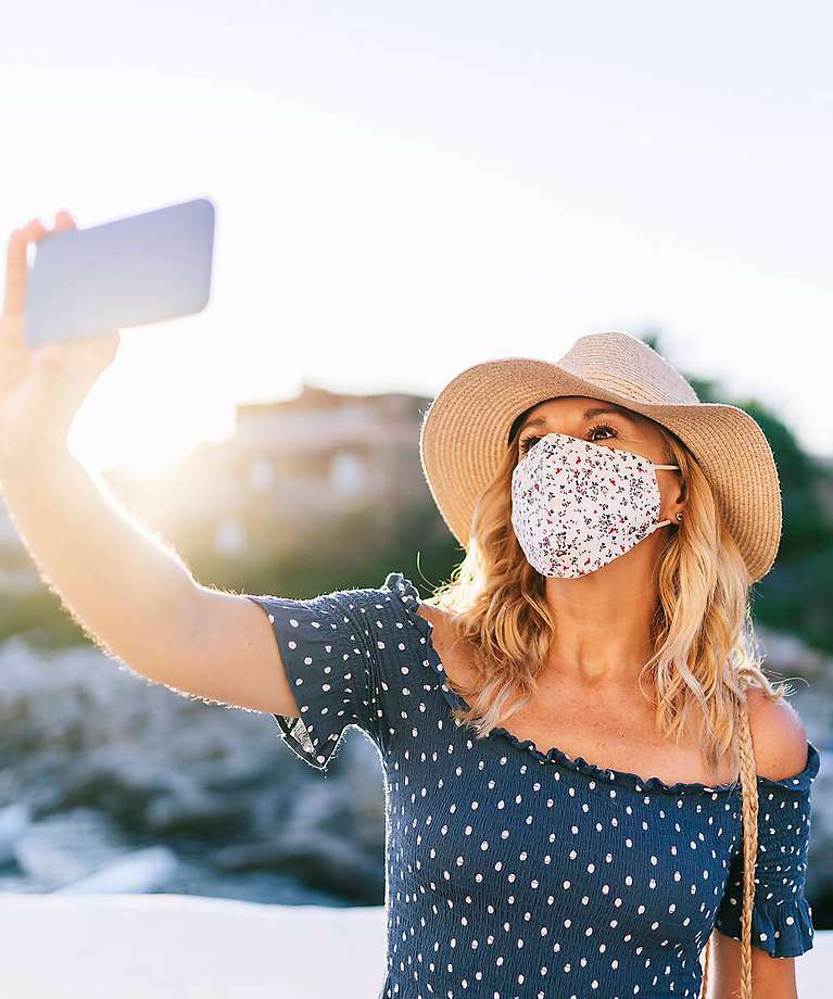Eine Frau trägt eine Mund-und Nasenschutz und nimmt ein Foto auf. 