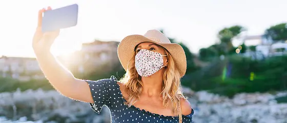 Eine Frau trägt eine Mund-und Nasenschutz und nimmt ein Foto auf. 