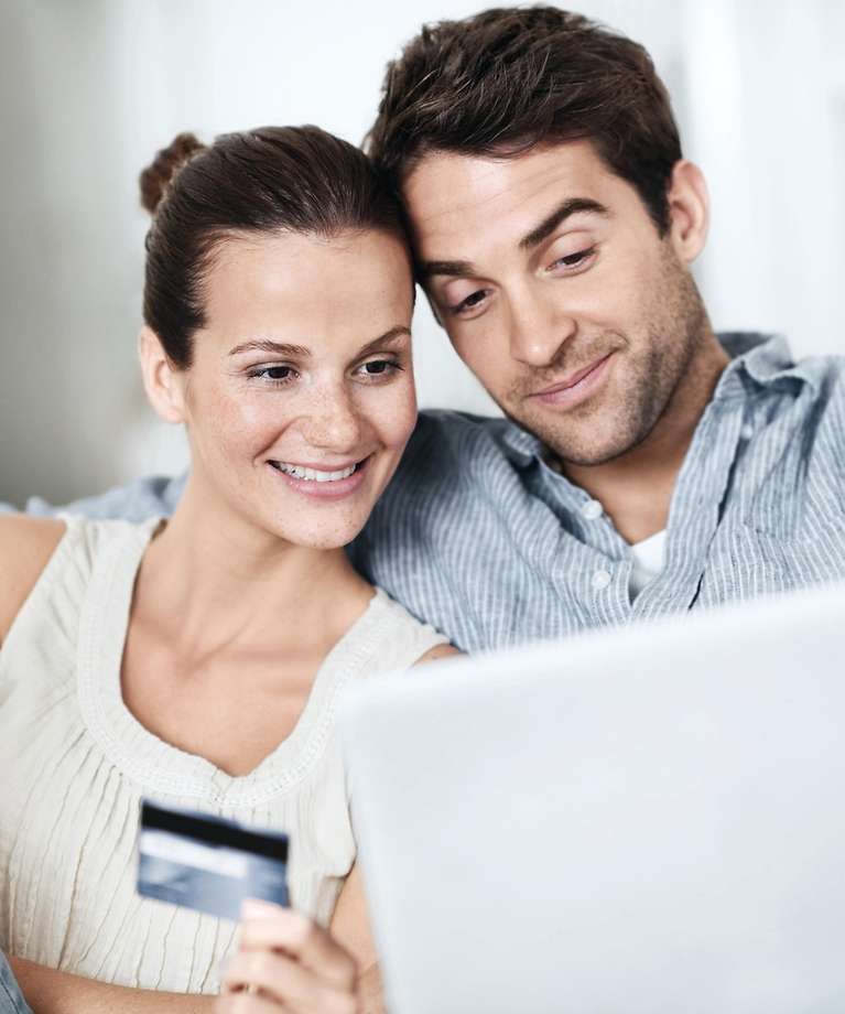 Eine Frau und ein Mann sitzen vor einem Laptop. Die Frau hält eine Kreditkarte in der Hand. 