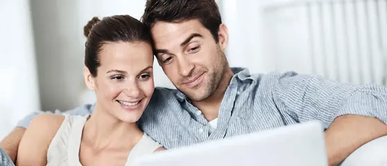 Eine Frau und ein Mann sitzen vor einem Laptop. Die Frau hält eine Kreditkarte in der Hand. 