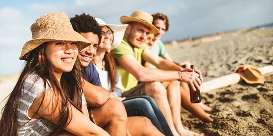 Sechs Freunde sitzen am Strand und genießen die Sonne.