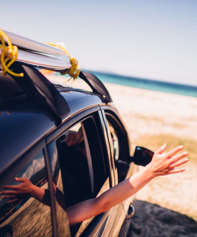 Ein Auto steht am Strand. Eine Person streckt ihren Arm aus dem Fenster. 