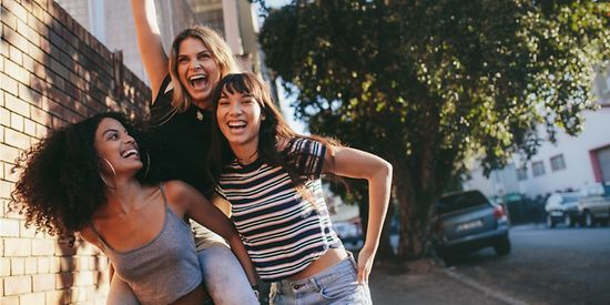 Drei junge Frauen stehen auf einem Fußweg und lachen.