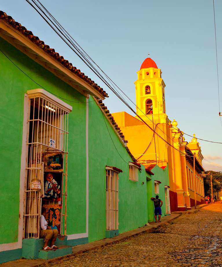 Ein Straße in Kuba. Auf der linken Seite ist ein grünes Gebäude und eine Kirche. 