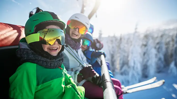 Eine Familie sitzt im Skilift. Im Hintergrund sind verschneite Bäume zusehen. 