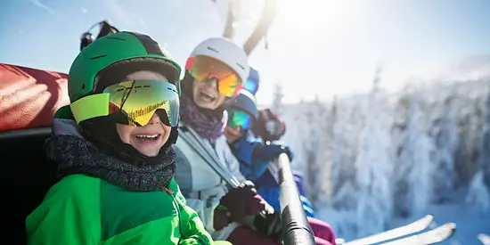 Eine Familie sitzt im Skilift. Im Hintergrund sind verschneite Bäume zusehen. 