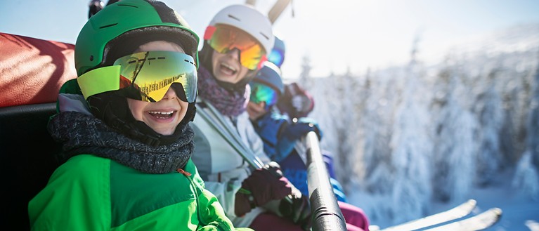 Eine Familie sitzt im Skilift. Im Hintergrund sind verschneite Bäume zusehen. 