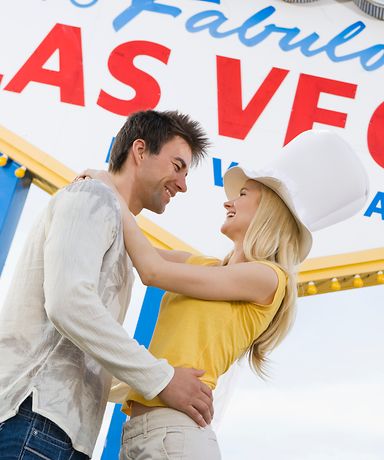 Ein Mann und eine Frau stehen vor einem großen Las Vegas Schild und lächeln sich an. 