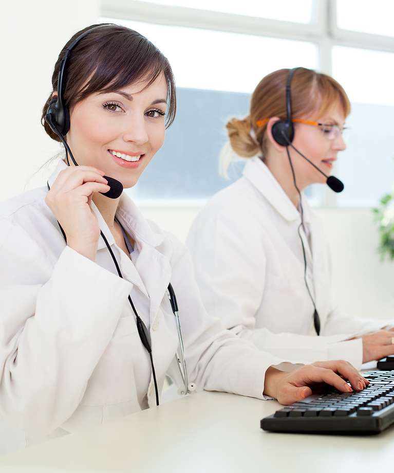 Zwei Frauen mit einem Headset sitzen am Computer und arbeiten. 