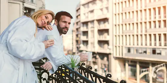 Zwei Personen stehen auf dem Balkon mit einem Kaffee in der Hand.