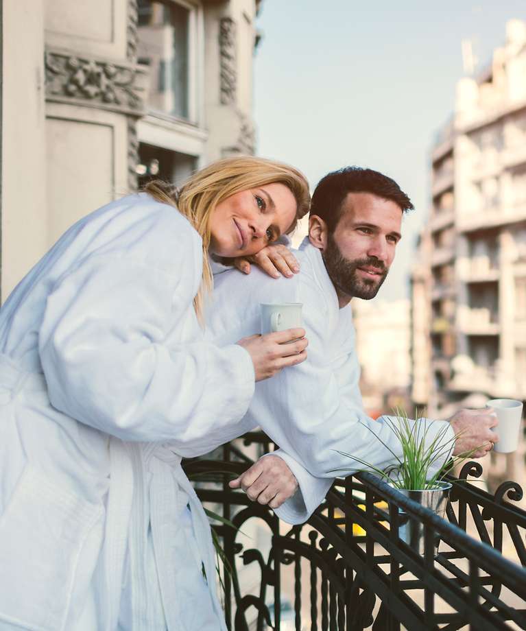Zwei Personen stehen auf dem Balkon mit einem Kaffee in der Hand.