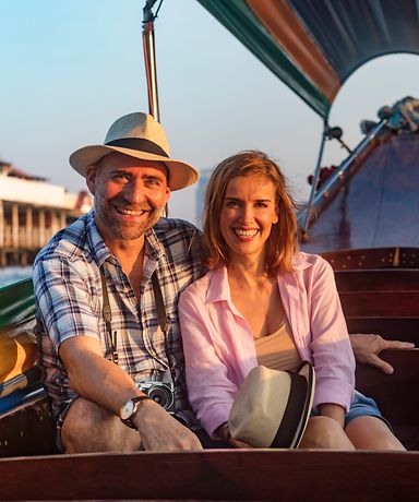 Ein Ehepaar sitzt auf einem Boot und lächelt in die Kamera.