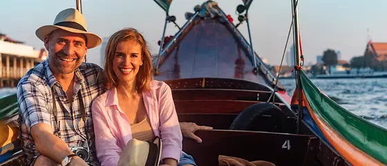 Ehepaar auf einem Boot - Jahres-Reiserücktrittsversicherung Ein Ehepaar sitzt auf einem Boot und lächelt in die Kamera.