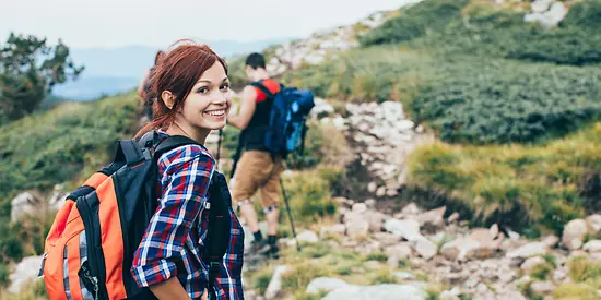 Eine Frau und ein Mann sind in den Bergen am Wandern. Die Frau lächelt in die Kamera.