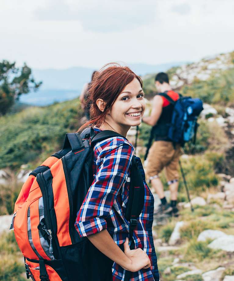 Eine Frau und ein Mann sind in den Bergen am Wandern. Die Frau lächelt in die Kamera.