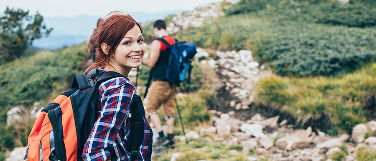 Eine Frau und ein Mann sind in den Bergen am Wandern. Die Frau lächelt in die Kamera.
