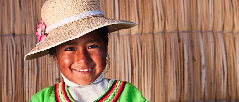 Ein bolivianisches Mädchen mit Hut das lächelt. 