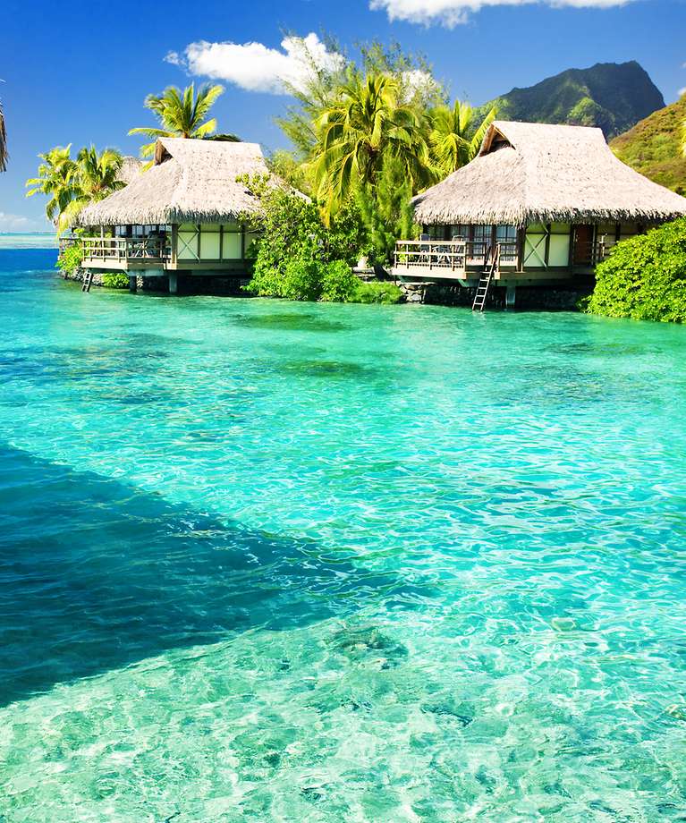 Man erkennt verschiedene Wasserbungalow, die umgeben sind von türkisem Wasser. 