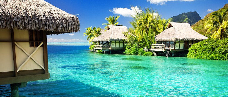 Man erkennt verschiedene Wasserbungalow, die umgeben sind von türkisem Wasser. 