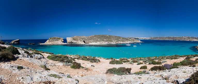Man erkennt eine Bucht mit türkisem Wasser. Im Hintergrund ist eine kleine Insel zu sehen. 