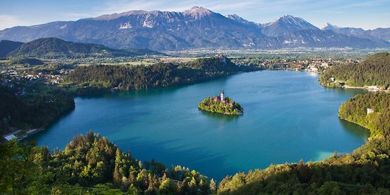 Man sieht einen großen See. In der Mitte des Sees befindet sich eine kleine Insel. Im Hintergrund sieht man eine Berglandschaft.