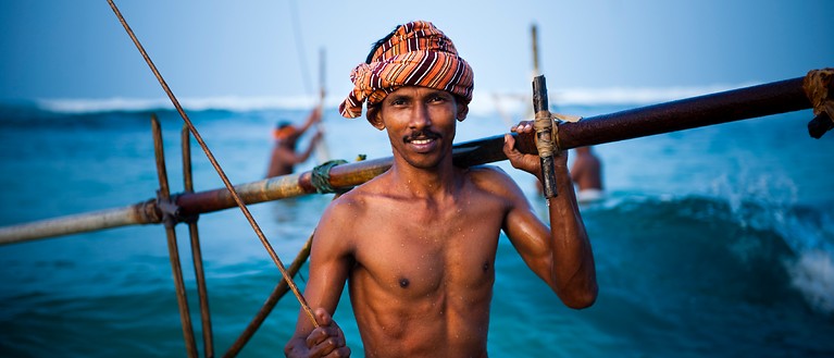 Man sieht einen Stelzenfischer, der im Meer steht und sein Equipment in der Hand hält.