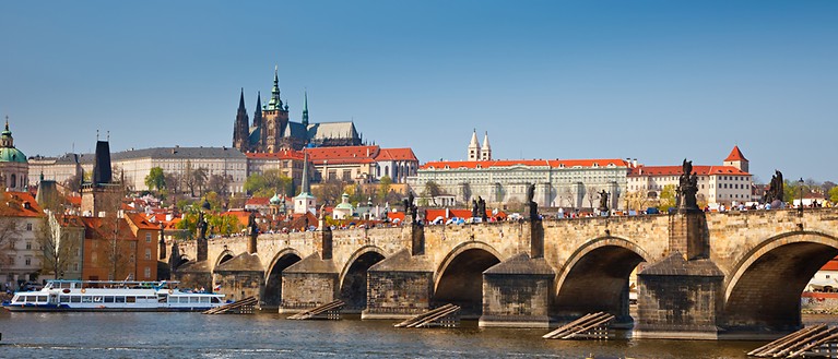 Man erkennt eine große gemauerte Brücke, die über einen Fluss ragt. Auf dem Fluss fahren Schiffe. Im Hintergrund sind Gebäude.