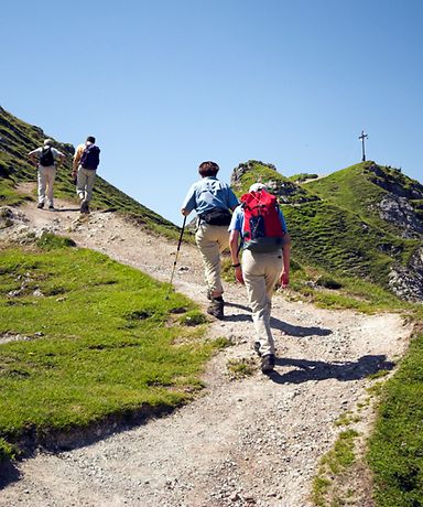 Man sieht mehrere Wanderer, die entlang eines Wanderwegs einen Berg erklimmen, um zur Spitze zu gelangen.