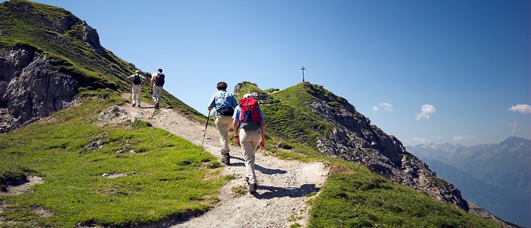 Man sieht mehrere Wanderer, die entlang eines Wanderwegs einen Berg erklimmen, um zur Spitze zu gelangen.