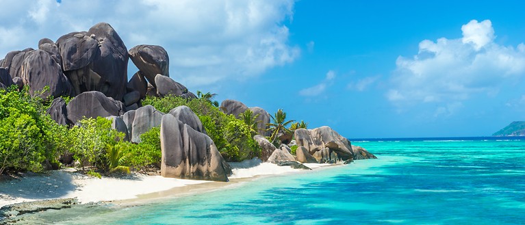 Man sieht einen Sandstrand mit Granitfelsen.