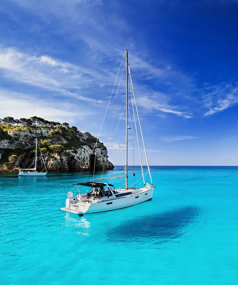 Ein kleines Segelschiff ankert in einer Bucht mit türkisfarbendes Wasser.
