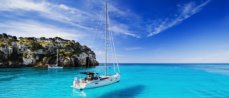 Ein kleines Segelschiff ankert in einer Bucht mit türkisfarbendes Wasser.