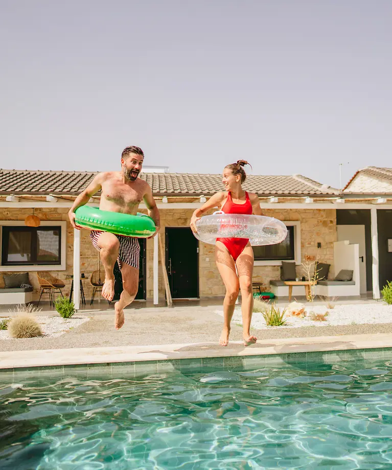 Ein Paar springt mit zwei Schwimmreifen in einen Pool.